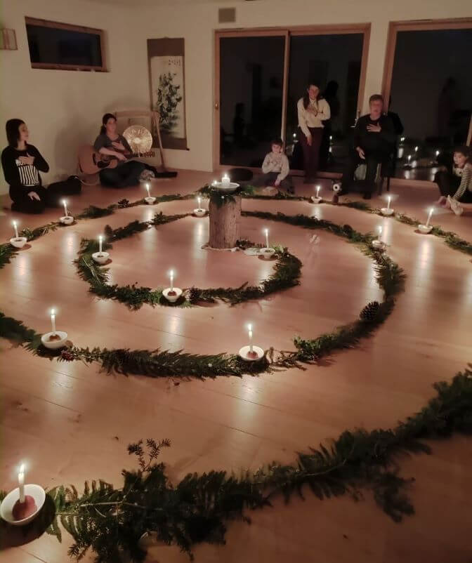 En soirée, une spirale dessinée avec des feuillages avec des bougies disposées régulièrement sur le tracé.